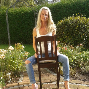 ältere Blondine sitzt auf einem Stuhl im Garten